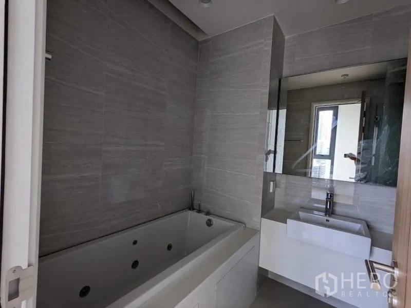 Condominium for sale - Contemporary bathroom with gray tiles, a large mirror, and a jetted bathtub.