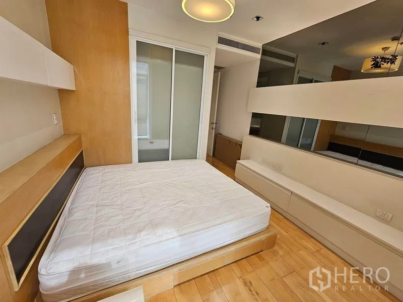 Condominium for rent or sale in Pathum Wan, Bangkok - Second bedroom with wood floors, built-in headboard and sliding glass wardrobe.