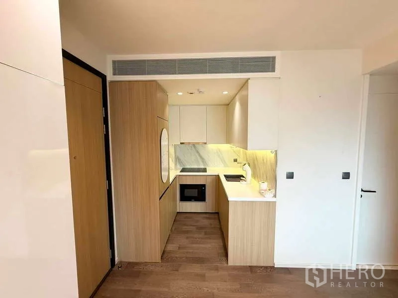 Condominium for rent in Watthana, Bangkok - Compact L-shaped kitchen with wood cabinetry, marble backsplash, and built-in appliances.
