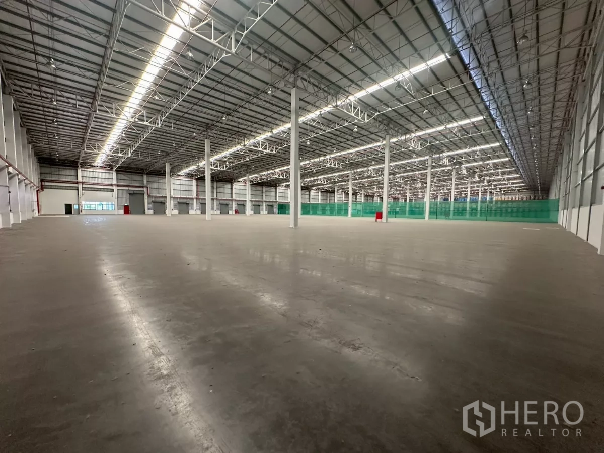 Warehouse for rent in Bang Phli, Samut Prakan - Deep warehouse bay showing long clear aisles and green safety netting partition.