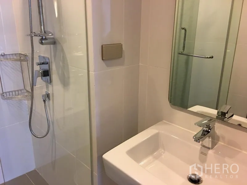 Condominium for rent in Watthana, Bangkok - Modern bathroom with glass-enclosed shower, chrome fixtures, vanity sink and mirror.