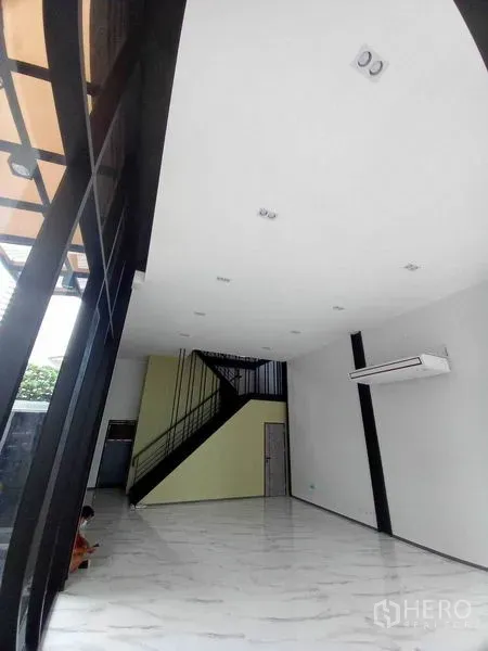 零售空间 出租在Khlong Toei, Bangkok - 挑高零售展厅，白色天花、仿大理石地面、黑色钢梯与壁挂空调，临街玻璃立面