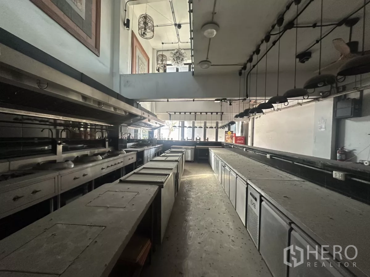 店屋 出租在Bang Na, Bangkok - 一层商用厨房，长条不锈钢备餐台与吊灯照明。