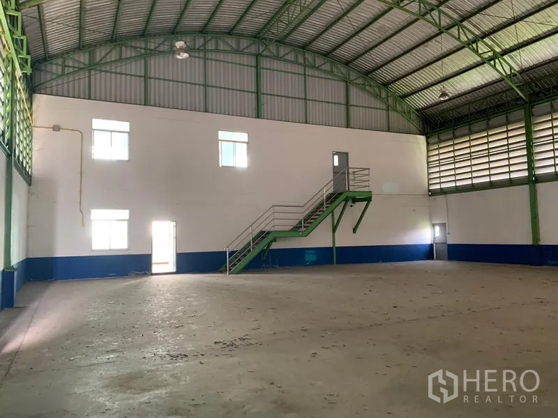 Warehouse for rent in Lam Luk Ka, Pathum Thani - Warehouse hall with high roof, concrete floor and a stairway leading to mezzanine office rooms.