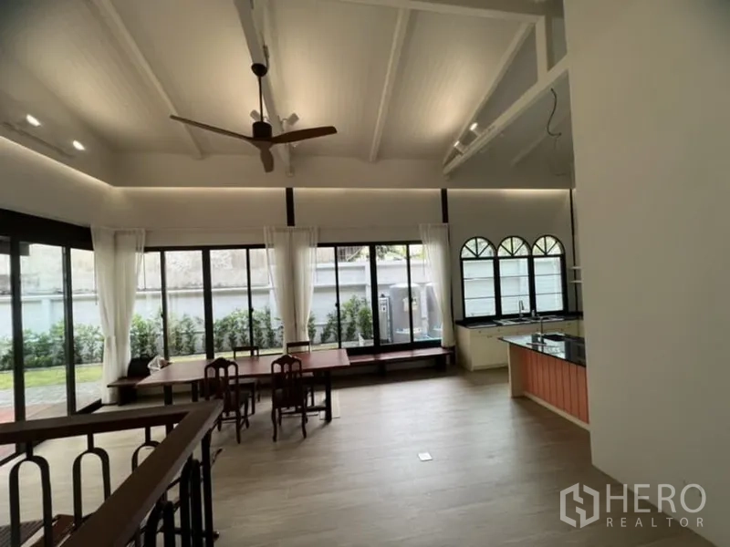 Detached House for rent in Ratchathewi, Bangkok - Double-height living room with vaulted ceiling, ceiling fan, large windows and an open kitchen.