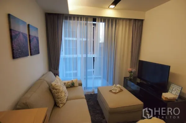 Condominium for rent in Pathum Wan, Bangkok - Cozy living room with sofa, ottoman and sheer curtains framing a full-height window.