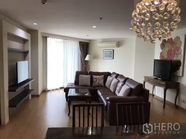 公寓 出租在Watthana, Bangkok - 采光良好的客厅，L形真皮沙发，大面积落地窗与窗帘，配电视柜和吊灯。