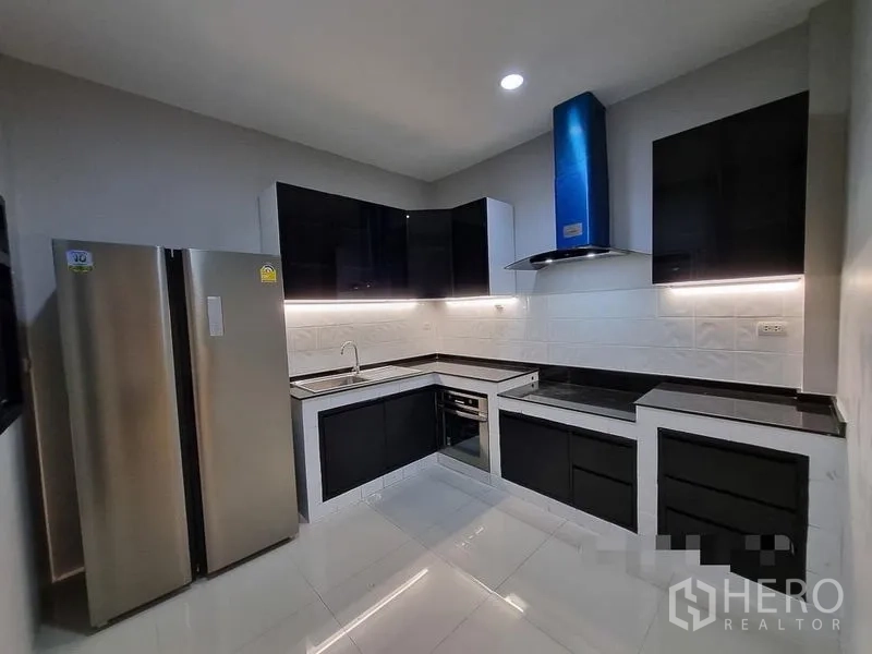 Detached House for rent in Bang Khae, Bangkok - Modern U-shaped kitchen with black cabinetry, stone counters, stainless fridge and range hood.