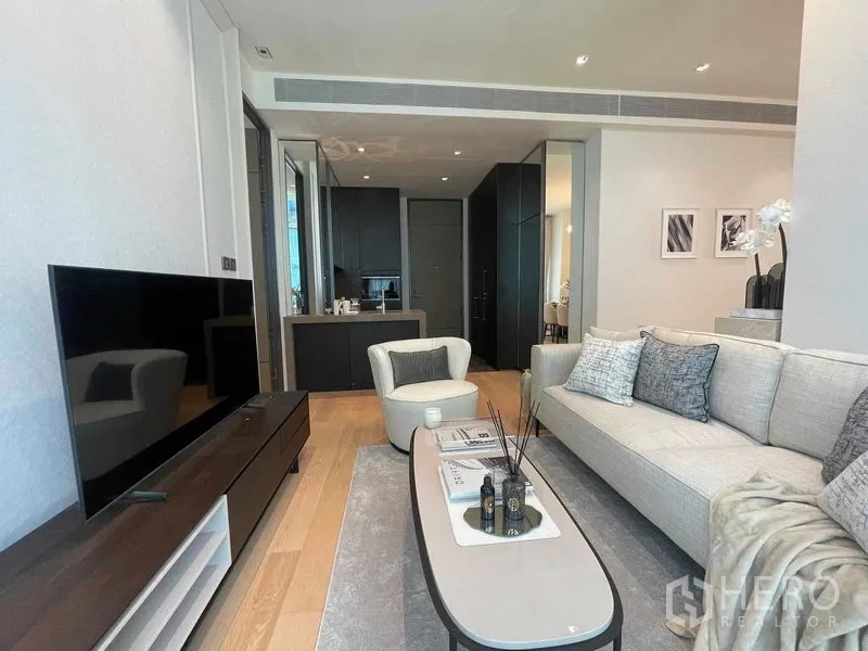 Condominium for rent in Pathum Wan, Bangkok - Living room facing the TV with sleek dark kitchen cabinetry and an island in the background.