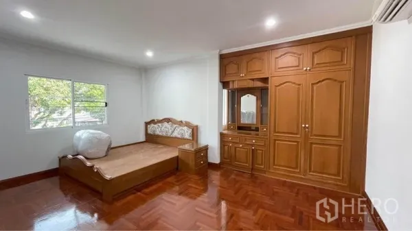 Detached House for rent in Bang Kapi, Bangkok - Spacious bedroom with built-in wooden wardrobe, bed frame and polished parquet flooring.