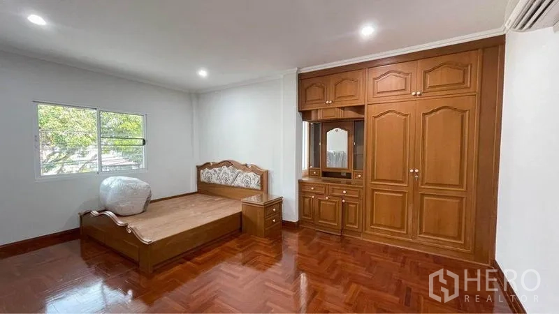 Detached House for rent in Bang Kapi, Bangkok - Spacious bedroom with built-in wooden wardrobe, bed frame and polished parquet flooring.