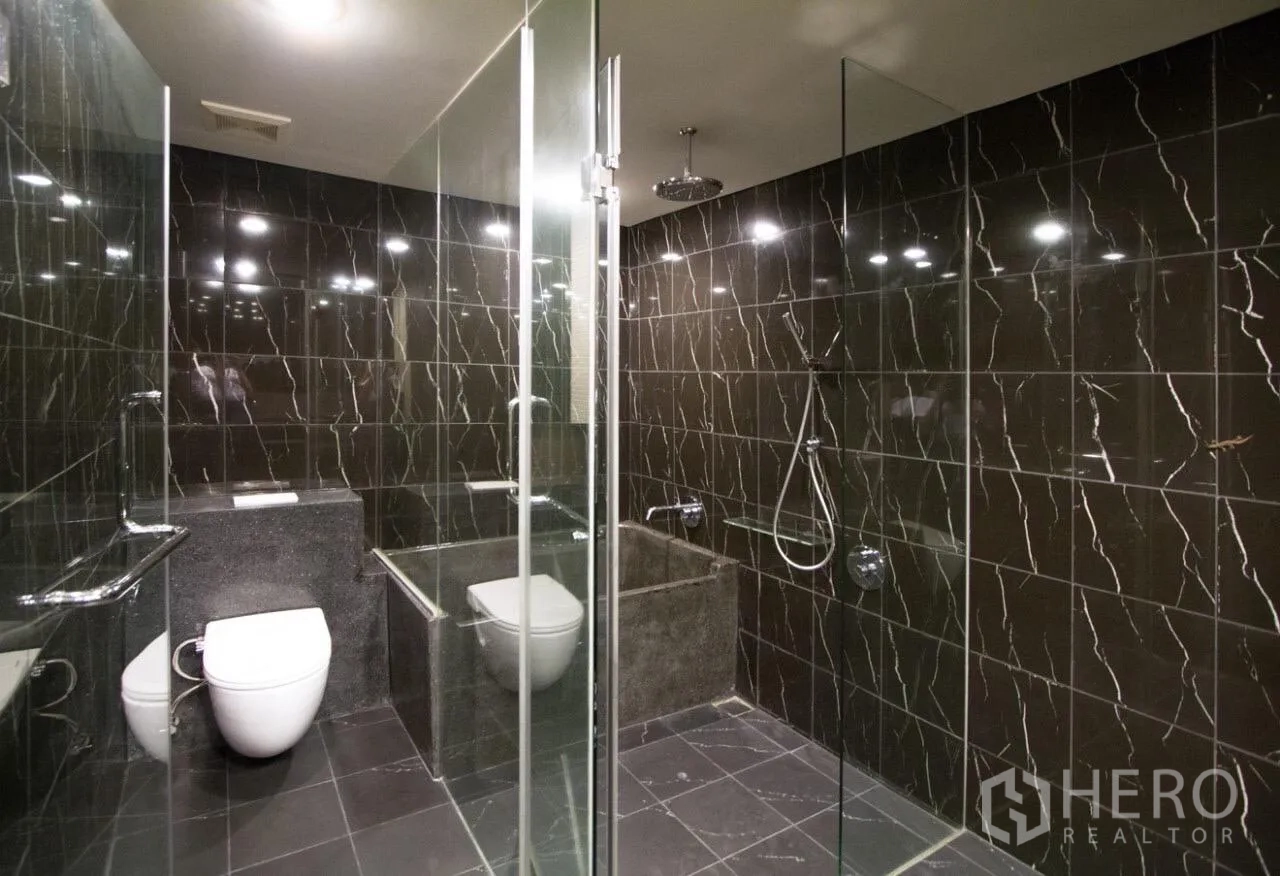 公寓 出租在Watthana, Bangkok - 宽敞浴室，深色大理石瓷砖与玻璃雨淋淋浴间。