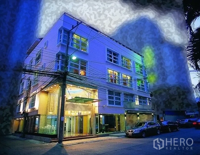 พื้นที่ขายปลีก ให้เช่า - อาคารมุมสมัยใหม่ยามค่ำ พร้อมหน้าร้านกระจกกว้างและที่จอดริมถนน