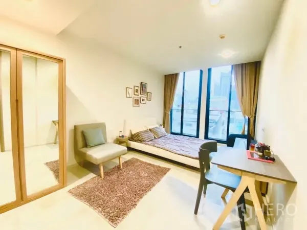 คอนโด ให้เช่าในPathum Wan, Bangkok - ห้องนอนวิวเมือง ผ่านหน้าต่างบานสูง พร้อมโต๊ะทำงาน ตู้เสื้อผ้าบานกระจก และเก้าอี้พักผ่อน