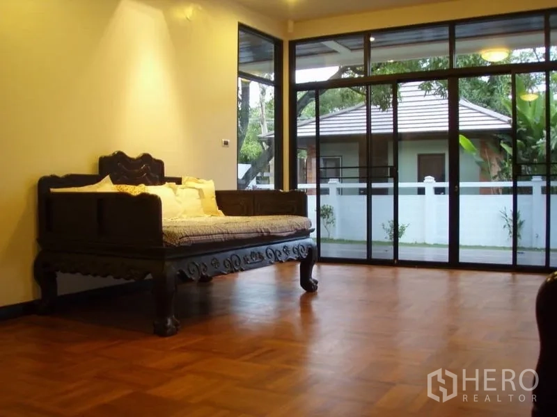 บ้าน ให้เช่าในHuai Khwang, Bangkok - ห้องนั่งเล่นกว้าง พื้นปาร์เกต์ เตียงไม้แกะสลัก และหน้าต่างสูงมองสวน