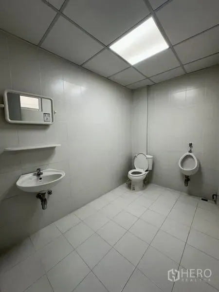 Office Space for rent in Khlong Toei, Bangkok - Clean tiled restroom with toilet, urinal, sink and bright ceiling light.