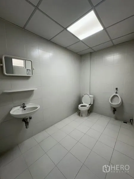 Office Space for rent in Khlong Toei, Bangkok - Clean tiled restroom with toilet, urinal, sink and bright ceiling light.