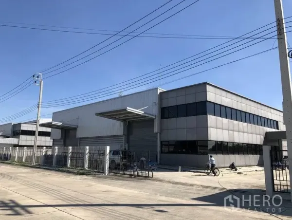 工厂 出租或出售在Bang Sao Thong, Samut Prakan - 现代化厂房外观，灰色金属幕墙，带雨棚装卸区、大型卷帘门与围栏入口，临宽阔道路。