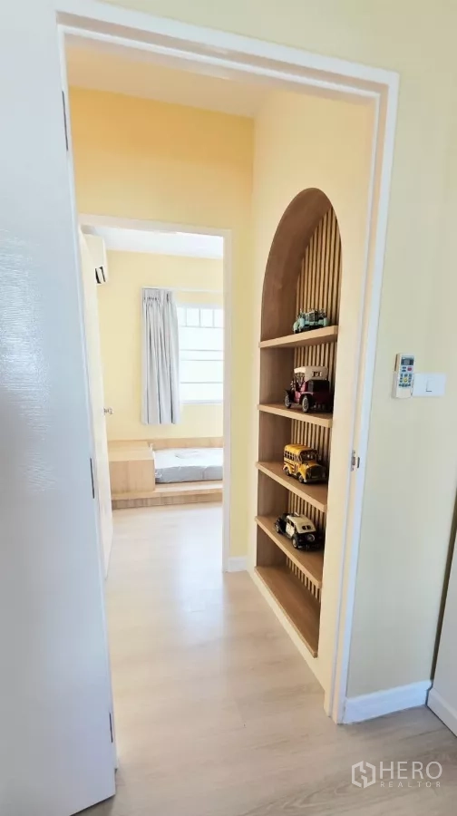 Townhouse for rent in Bang Bo, Samut Prakan - Corridor with arched niche shelving and wood floors leading to bedroom.