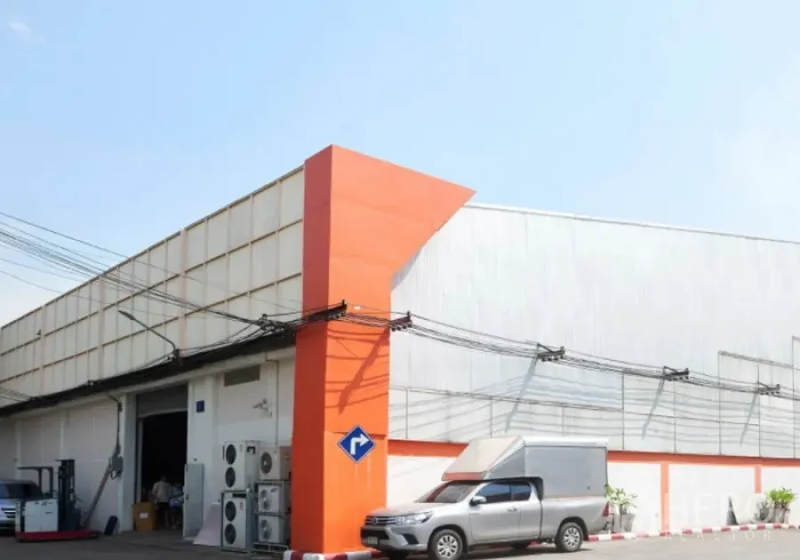 Warehouse for rent in Bang Na, Bangkok - Corner view of a modern warehouse facade with orange accent and front parking area.