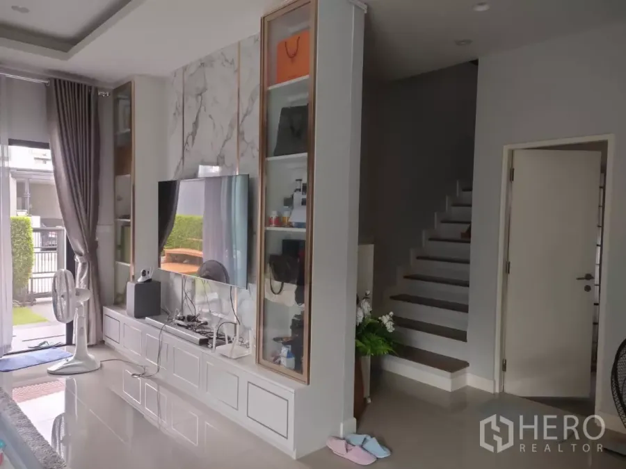 บ้าน ให้เช่าหรือขายในLam Luk Ka, Pathum Thani - ห้องนั่งเล่นสไตล์โมเดิร์น ผนังทีวีลายหินอ่อน ตู้บิลท์อิน และบันไดข้างประตูกระจกบานเลื่อน