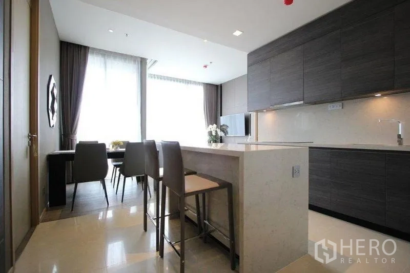 Condominium for rent in Watthana, Bangkok - Open kitchen with breakfast island and two bar stools facing large windows.