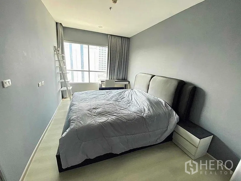 คอนโด ขายในHuai Khwang, Bangkok - ห้องนอนกว้าง เตียงหัวเตียงบุนวม โต๊ะข้างเตียง และโต๊ะทำงานริมหน้าต่าง