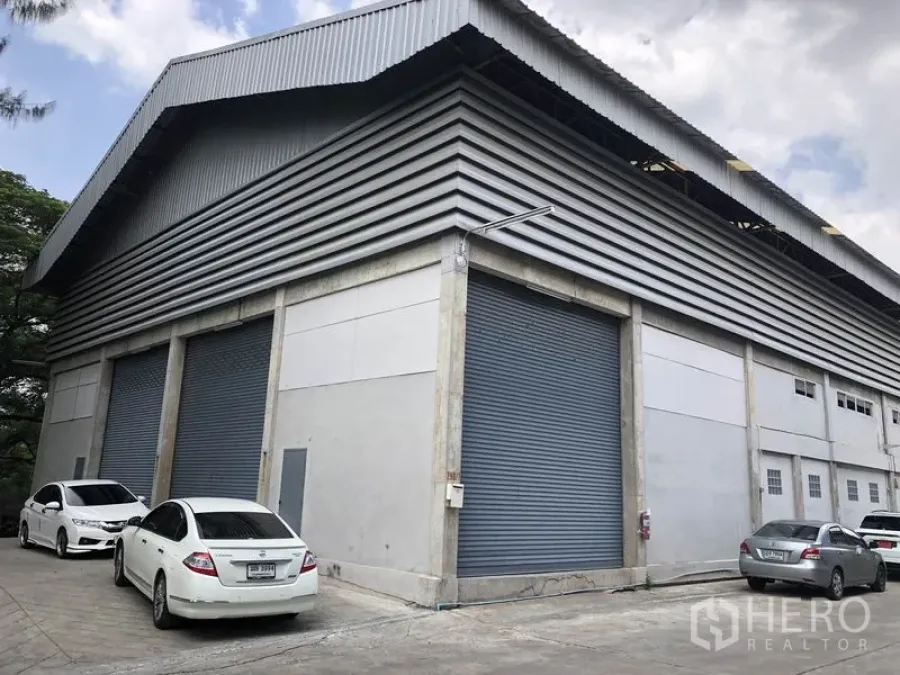 货栈 出租在Khlong Sam Wa, Bangkok - Khlong Sam Wa 工业仓库转角外观，金属包板与高屋顶，多个卷闸门及停车位。