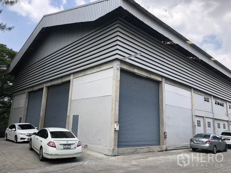 货栈 出租在Khlong Sam Wa, Bangkok - Khlong Sam Wa 工业仓库转角外观，金属包板与高屋顶，多个卷闸门及停车位。