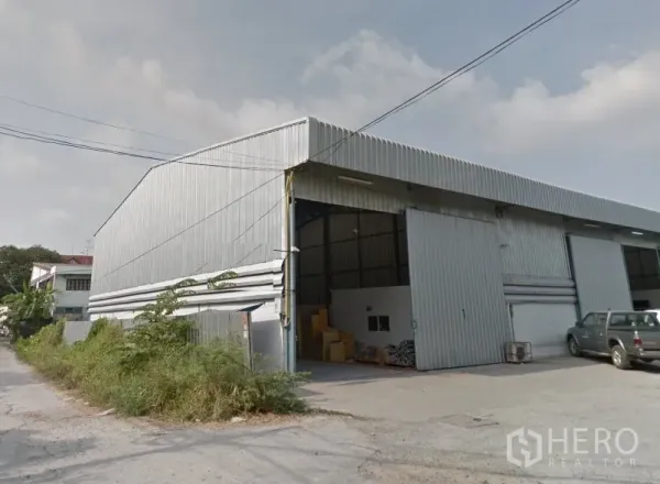 货栈 出租在Pak Kret, Nonthaburi - Pak Kret金属板外墙仓库外观，高挑人字形屋顶，宽大滑动门与前方混凝土装卸区