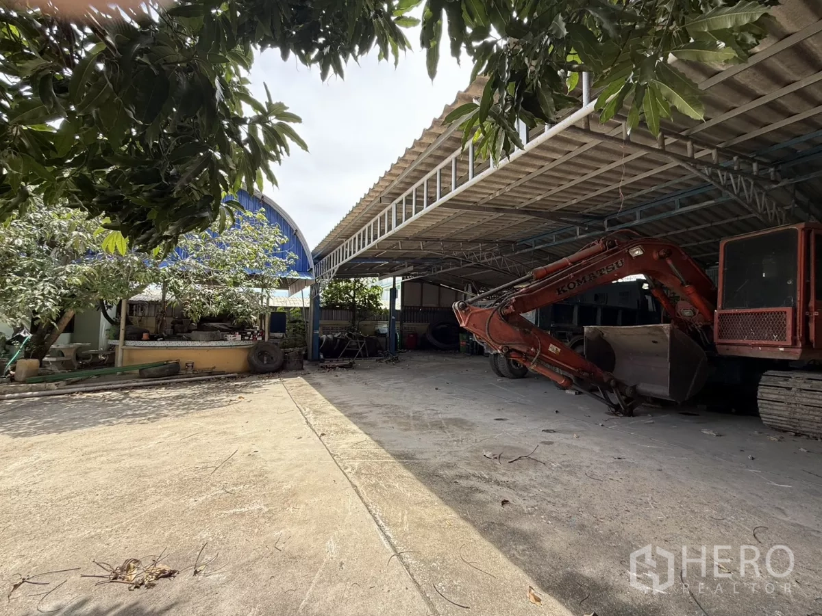 Warehouse for sale in Phra Samut Chedi, Samut Prakan - Open concrete yard with trees and workshop buildings around the boundary.