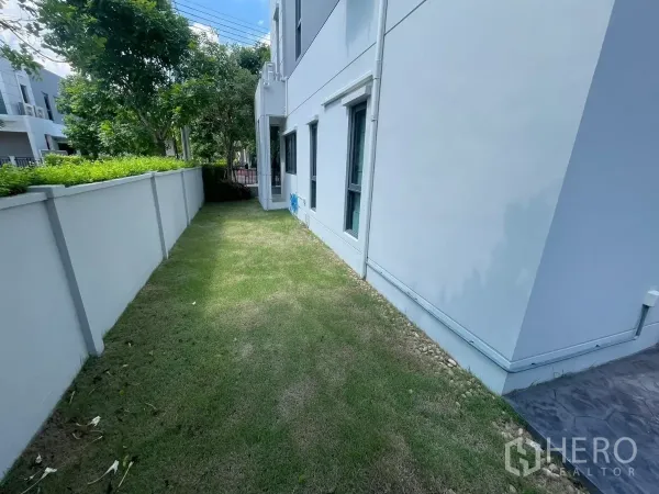 独立式住宅 出租在Bang Phli, Samut Prakan - 房屋侧边草坪，私密围墙与成树环绕。