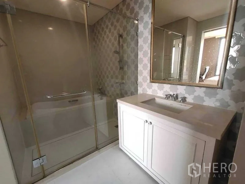 Condominium for sale in Khlong Toei, Bangkok - Modern bathroom with glass-enclosed shower and a large vanity with mirror.