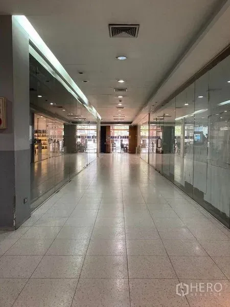 พื้นที่ขายปลีก ให้เช่า - ทางเดินห้างยาว มีหน้าร้านกระจกสองฝั่ง ไฟดาวน์ไลท์และช่องแอร์ มุ่งสู่ทางเข้า