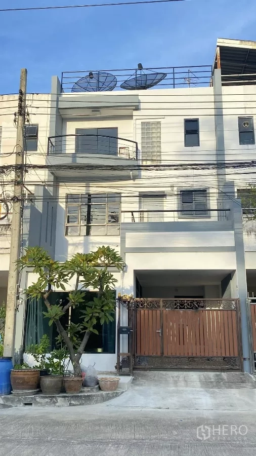 带办公室的家 出租在Bang Na, Bangkok - 三层家庭办公楼外立面，带阳台、带门庭院车位、屋顶天线与盆栽。