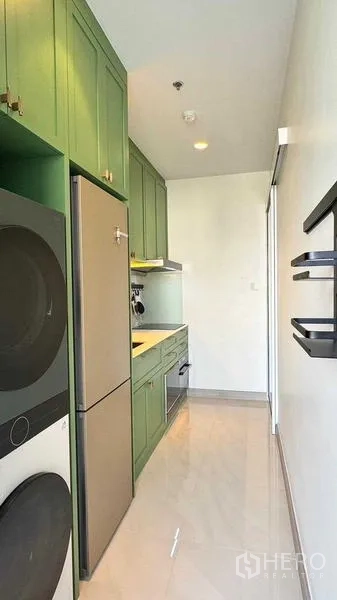 Condominium for rent in Bang Rak, Bangkok - Narrow kitchen with green cabinets, stacked washer and dryer, refrigerator and glossy white floor tiles.