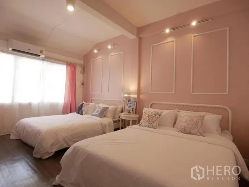 Townhouse for rent in Khlong Toei, Bangkok - Second bedroom with a pastel pink feature wall, two double beds, spot lighting and a curtained window.