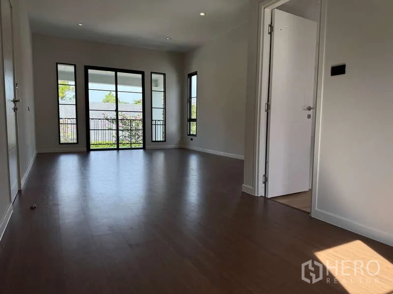 Detached House for rent or sale in Bang Phli, Samut Prakan - Spacious upper room with balcony doors and tall windows overlooking greenery.