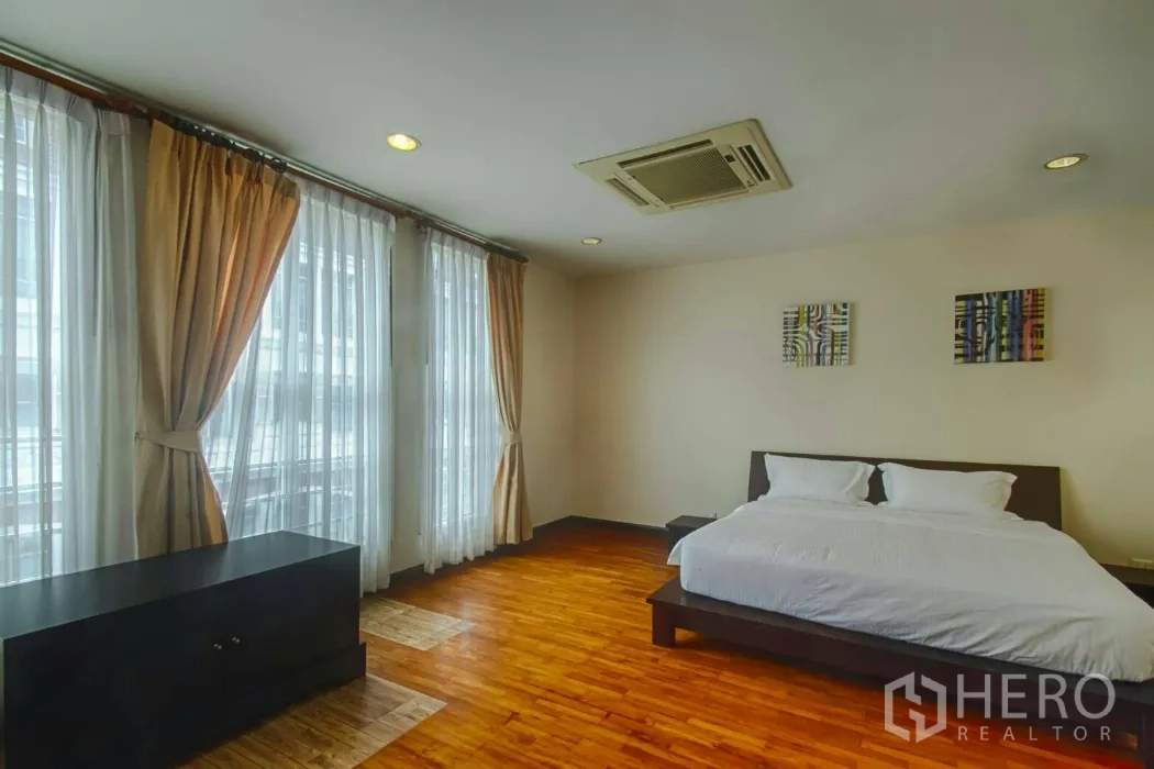 Townhouse for rent in Watthana, Bangkok - Bright bedroom with wall-to-wall windows, sheer curtains and wood flooring.