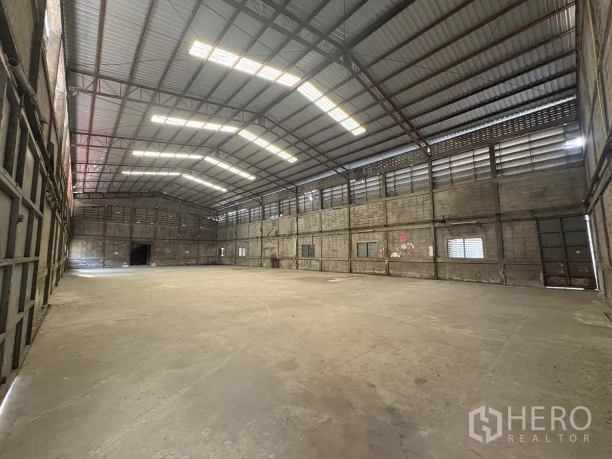 Warehouse for rent in Khlong Toei, Bangkok - Large warehouse bay with wide‑span roof, side windows, and a loading door at the far end.
