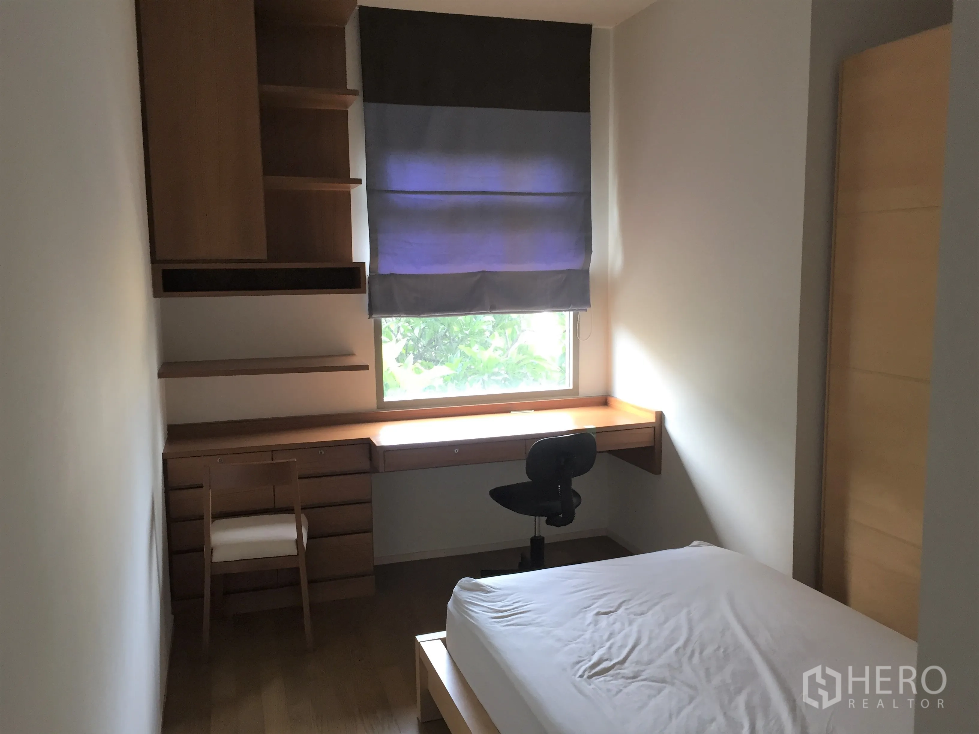 Condominium for rent in Watthana, Bangkok - Second bedroom with single bed, built‑in desk and shelves, Roman blind and leafy window view.