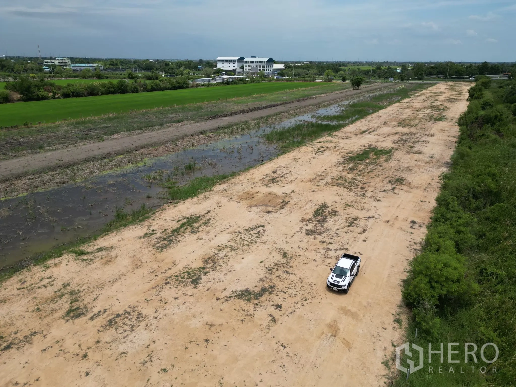 Land for sale in Sai Noi, Nonthaburi - Closer aerial showing leveled ground with a car on site and drainage channels along the plot.