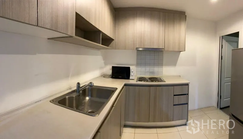 Condominium for rent - Fitted kitchen with light wood cabinets, sink, cooktop, and microwave.