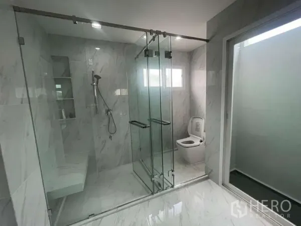 Detached House for rent or sale in Bang Bua Thong, Nonthaburi - Contemporary bathroom with marble tiles, glass-enclosed shower with bench, and separate toilet area.