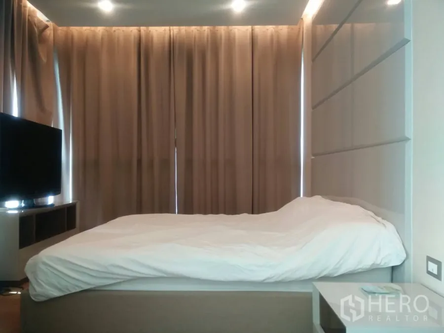 Condominium for rent in Ratchathewi, Bangkok - Cozy master bedroom with upholstered headboard, TV console and floor-to-ceiling blackout curtains in a Bangkok condo