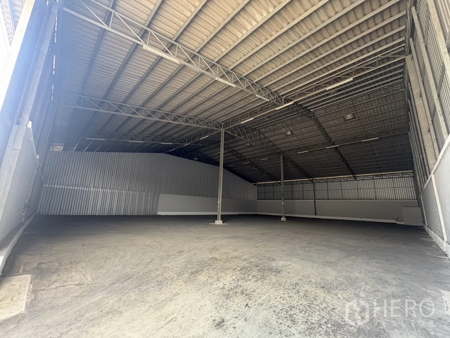 Warehouse for rent in Samut Prakan - Wide-span warehouse interior with high corrugated roof, steel trusses and concrete floor.