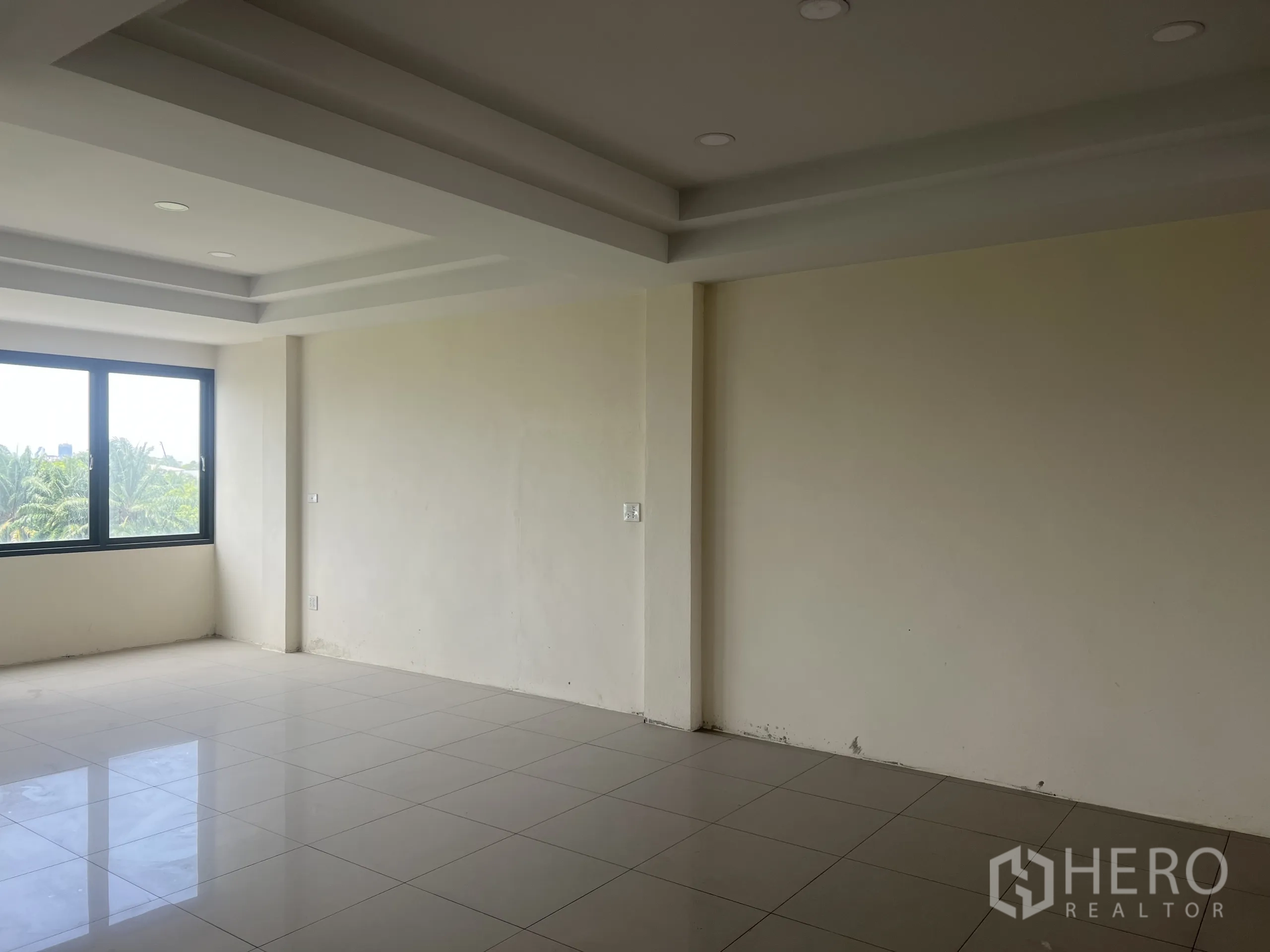 Home Office for rent in Suan Luang, Bangkok - Empty room with tray ceiling, glossy tiles and a large window facing greenery.