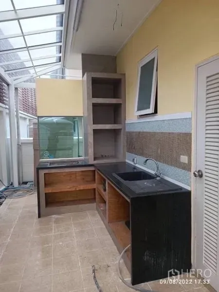 独立式住宅 出售在Prawet, Bangkok - 半室外泰式厨房，黑色台面、水槽与置物架，采光屋顶。