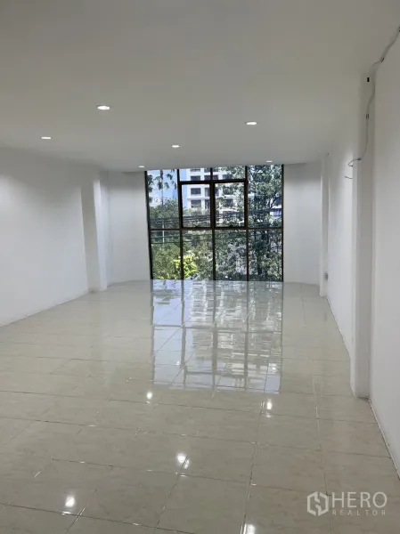 Shophouse for rent in Watthana, Bangkok - Bright upper-floor room with glossy tiles and a large window overlooking greenery.