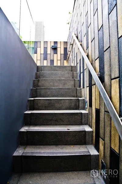 Condominium for rent in Watthana, Bangkok - Outdoor concrete staircase with patterned wall cladding and metal handrail.